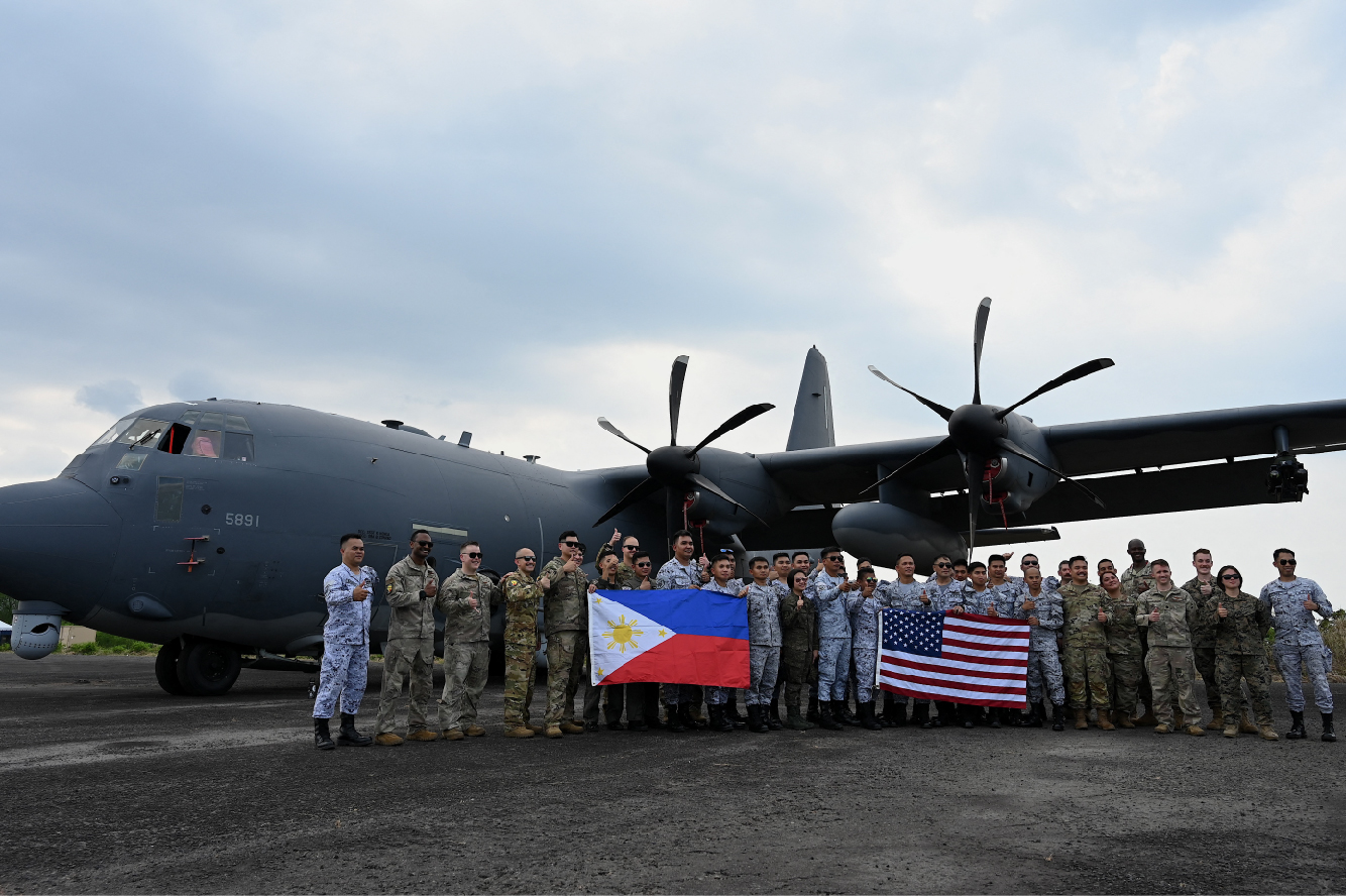 U.S. and Philippine troops stand together holding their respective countries' flags in front of a plane during a joint military exercise.