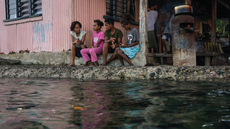 Children sit next to a flooded sea wall during high tide in Serua Village, Fiji.