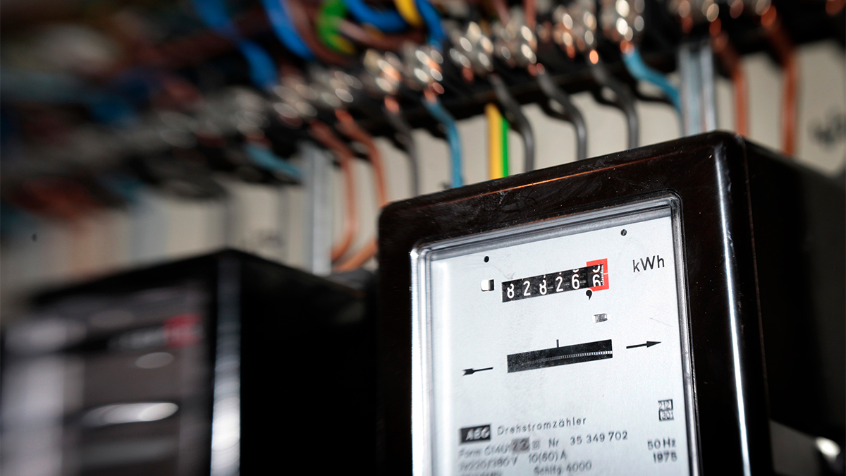 Electricity meter box displaying a reading for kilowatt hours, connected to wires on a wall.