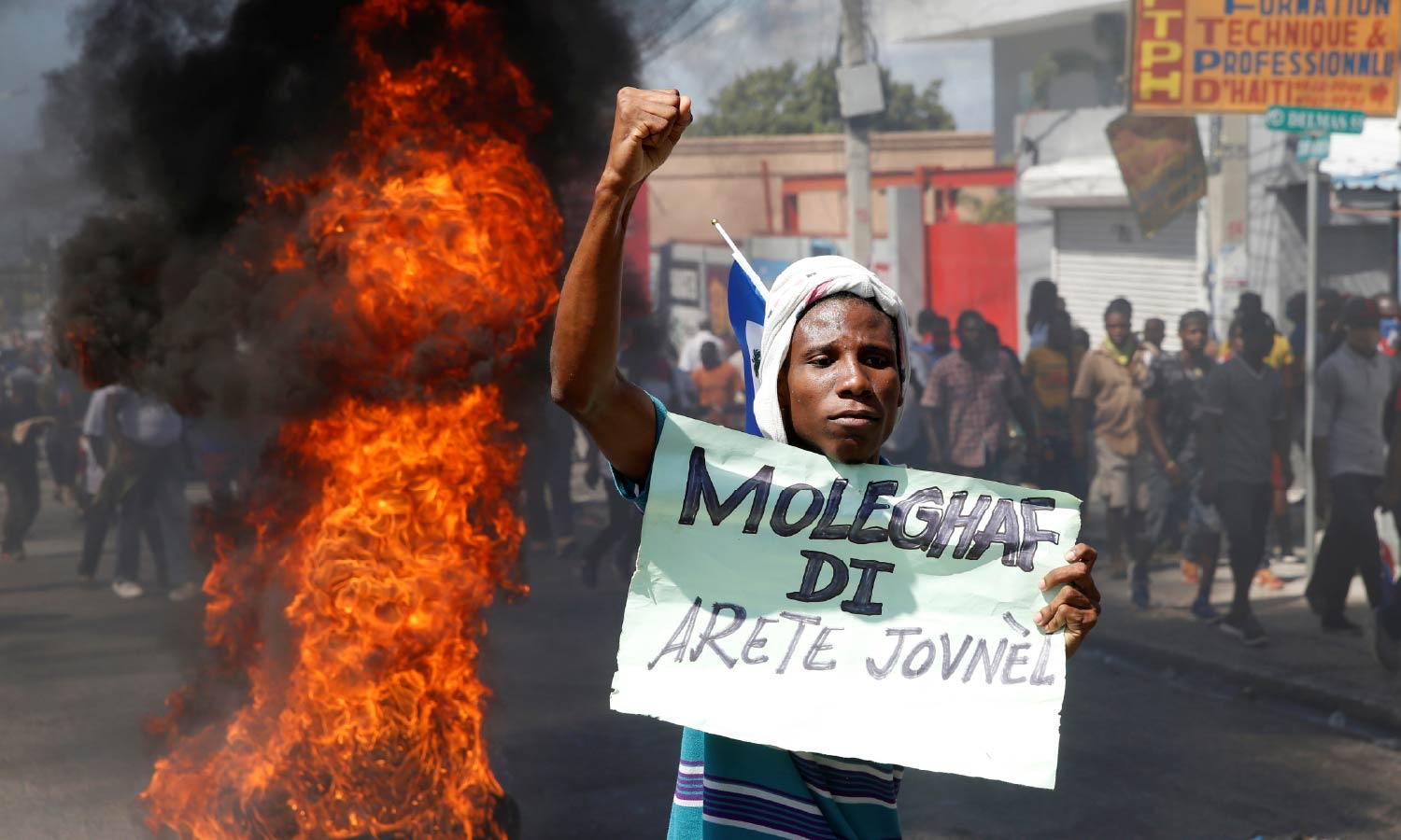 A Haitian demonstrator gestures while holding a sign near a barricade during a protest against Haiti's President Jovenel Moise.