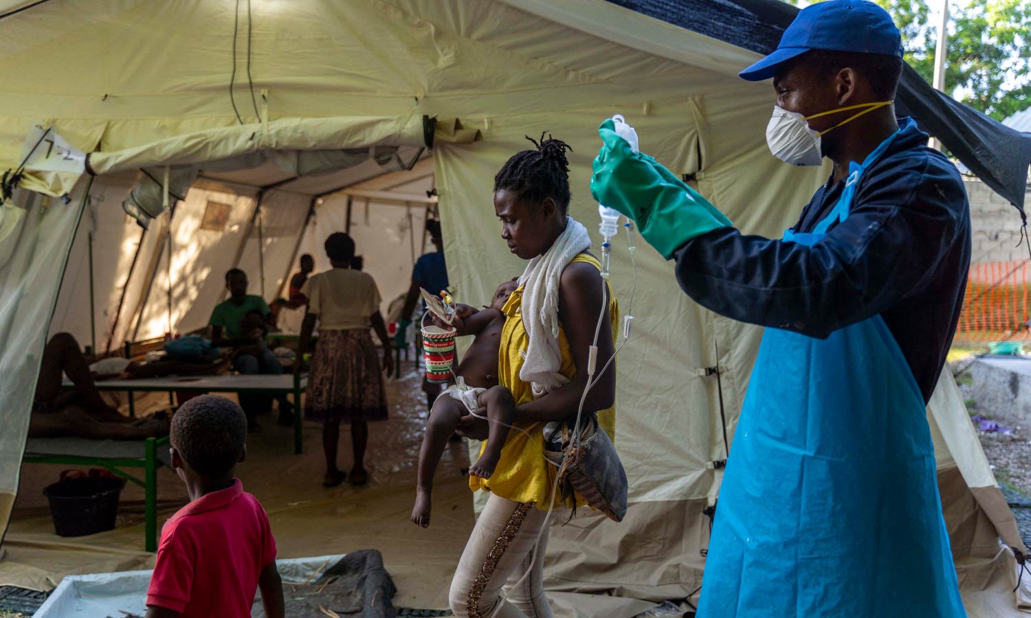 A woman brings her child showing symptoms of cholera to receive treatment at a clinic run by Doctors Without Borders as a medical worker sets up equipment.