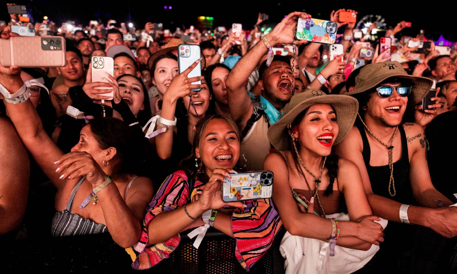 A large crowd of fans with their phones in their hands recording the stage watch Bad Bunny performing onstage at the Coachella music festival.