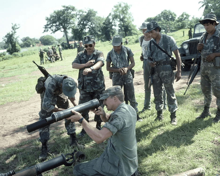 A U.S. Army trainer (center) examines part of a rifle during target practice with Salvadoran Army soldiers in San Miguel, El Salvador.
