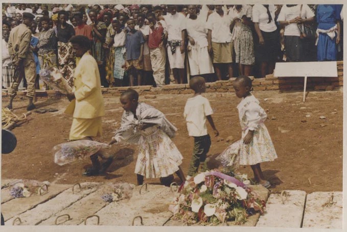An undated image shows three children and a woman laying wreaths on a mass grave of genocide victims in Rwanda