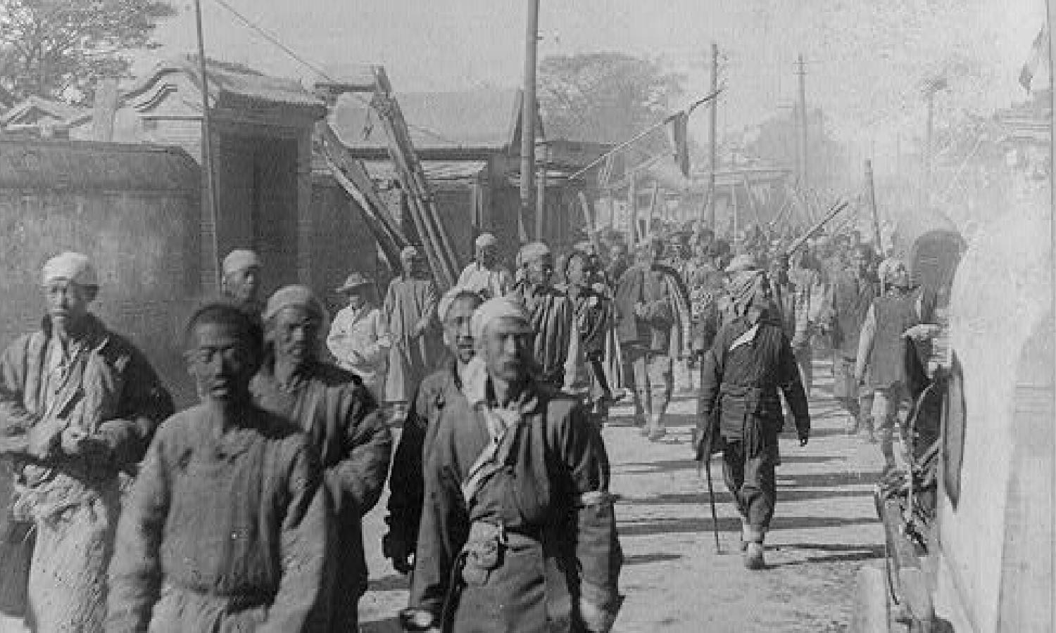 Black and white photo of Chinese men walking in dirt street circa 1901.