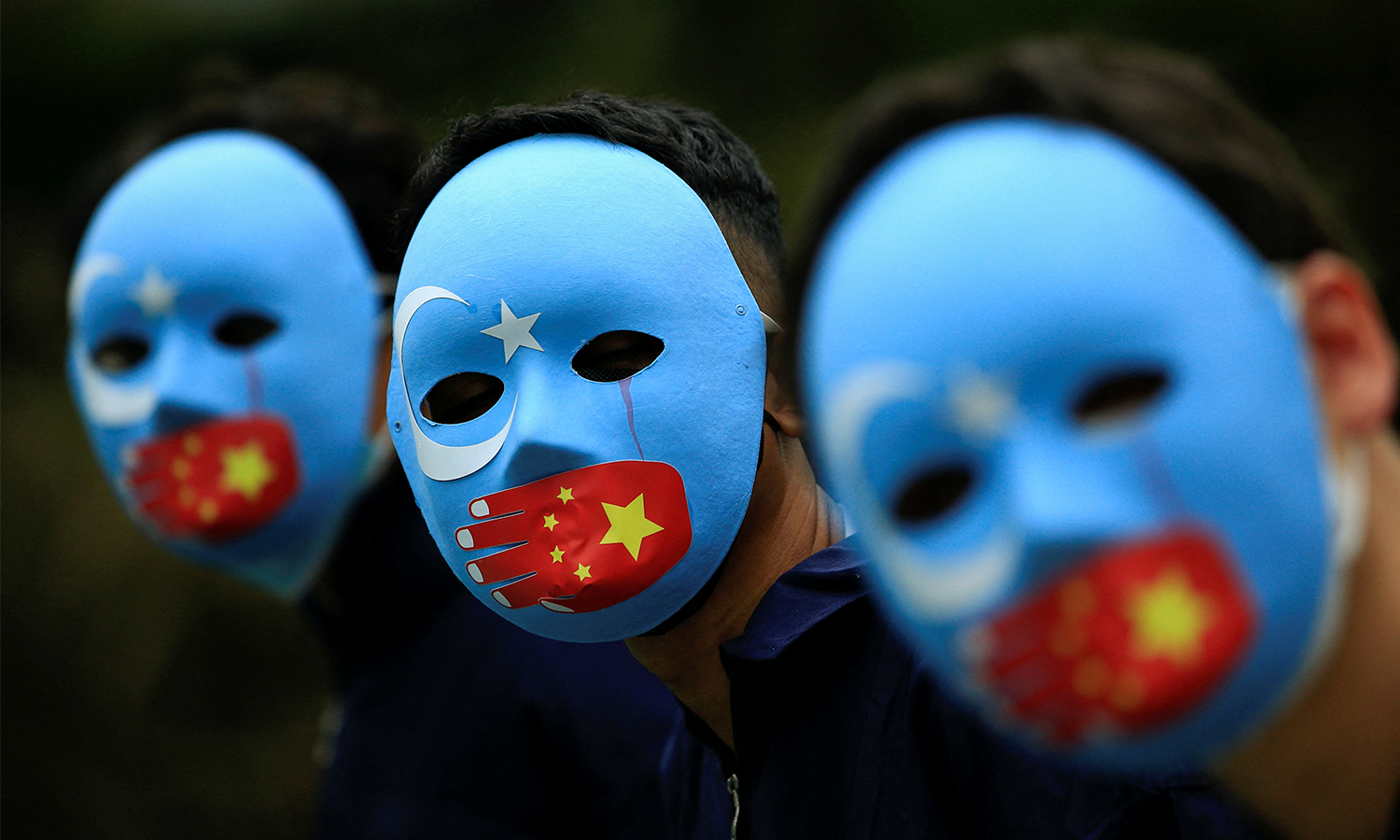 Activists wearing blue masks showing the flag of East Turkestan covered by a hand showing the Chinese flag, protest against China's treatment towards the ethnic Uyghurs.