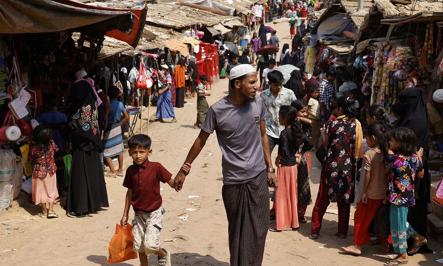 A Rohingya refugee man walks and holds a child's hand in a market, at the Rohingya refugee camp in Cox's Bazar, Bangladesh.