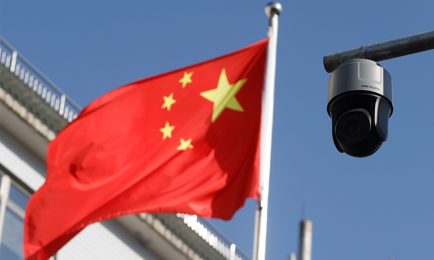 A security surveillance camera overlooking a street is pictured next to a nearby fluttering flag of China in Beijing, China on November 25, 2021.
