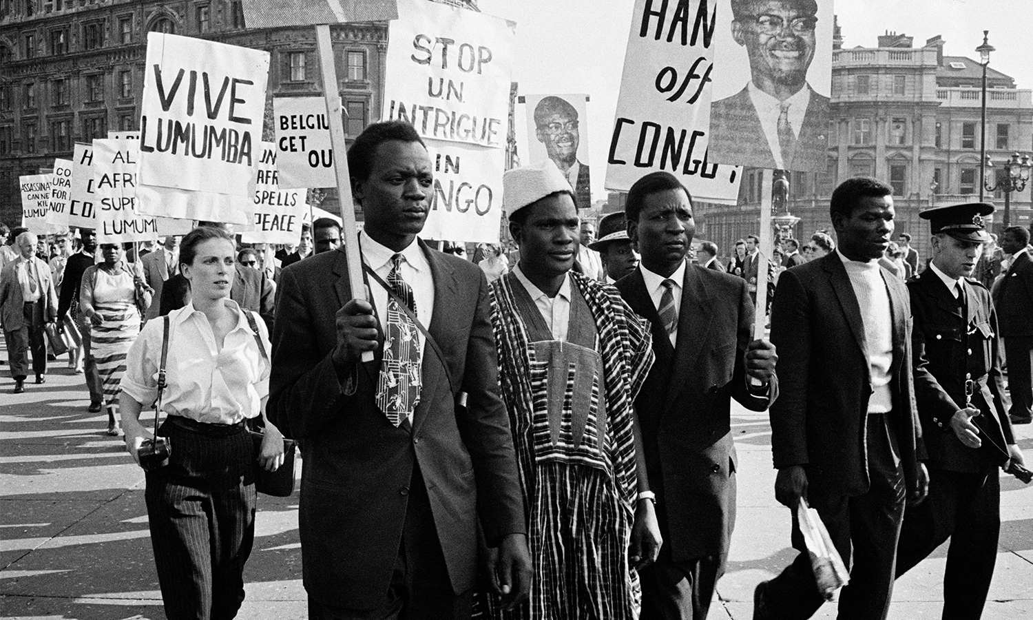Black and white photo of Black and white protesters marching with signs reading "Vive Lumumba" and "Hands off Congo."