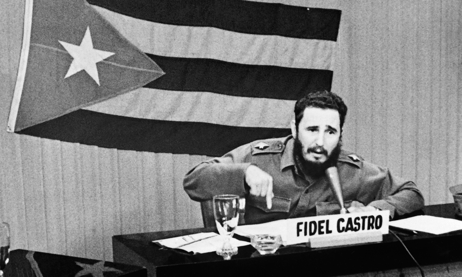 Fidel Castro speaks into a microphone in front of a Cuban flag.