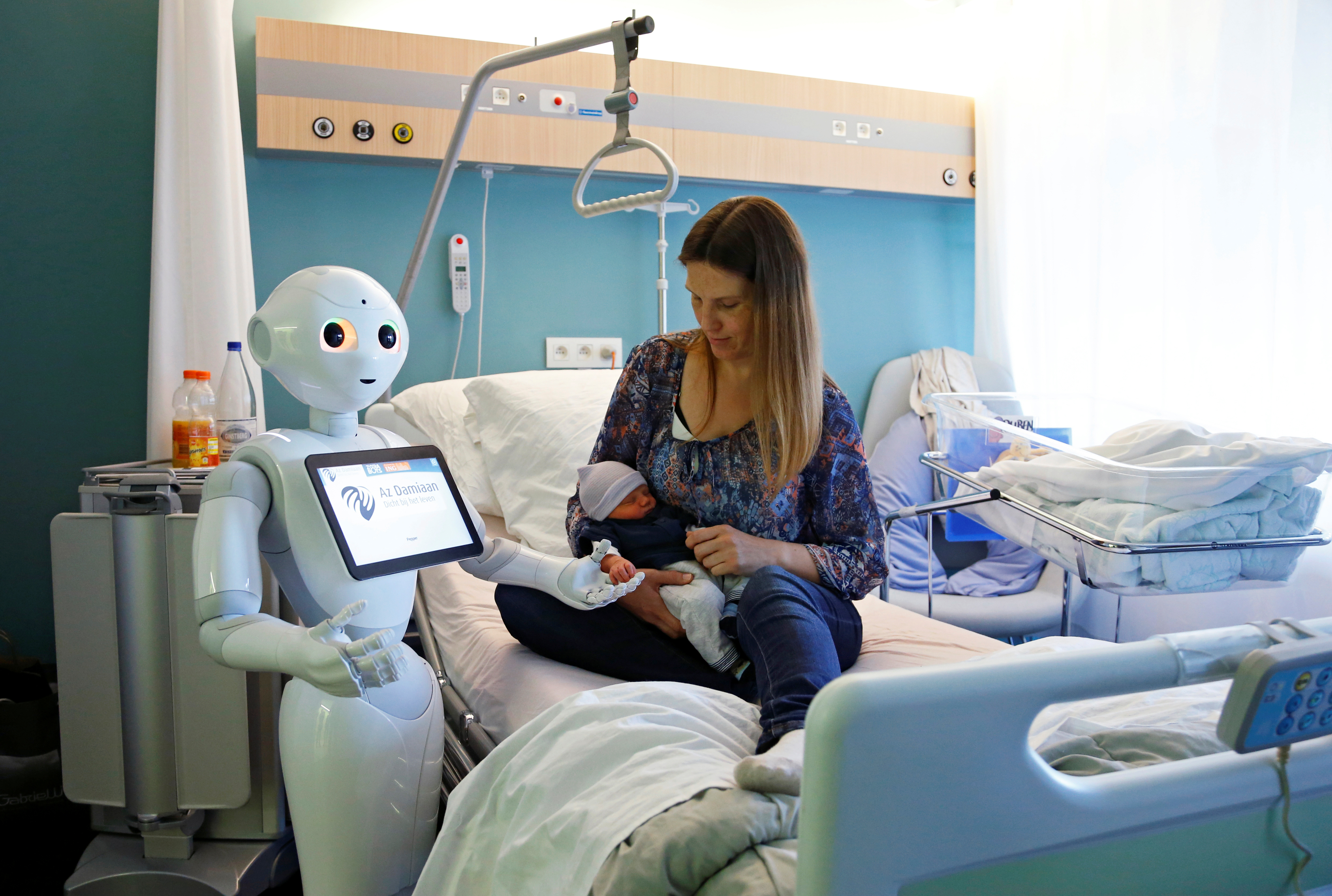 “Pepper” the robot, a humanoid robot designed to welcome and take care of visitors and patients, holds the hand of a newborn baby next to his mother at AZ Damiaan hospital in Ostend, Belgium, on June 16, 2016. Source: Francois Lenoir/Reuters.