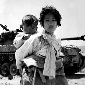 With her brother on her back, a Korean girl trudges by a stalled M-26 tank in Haengju, Korea, in 1951.