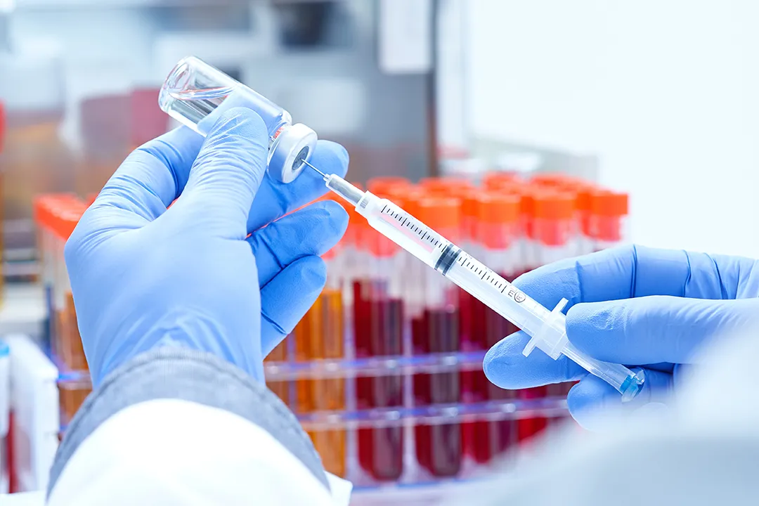 Close-up on doctor's hands, wearing blue protective gloves, dialing medicine into syringe from a vaccine vial. 