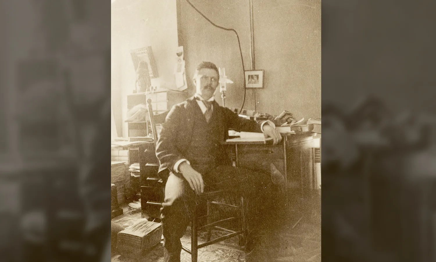 A sepia colored photograph of William Jennings Bryan standing in a suit next to the American flag.