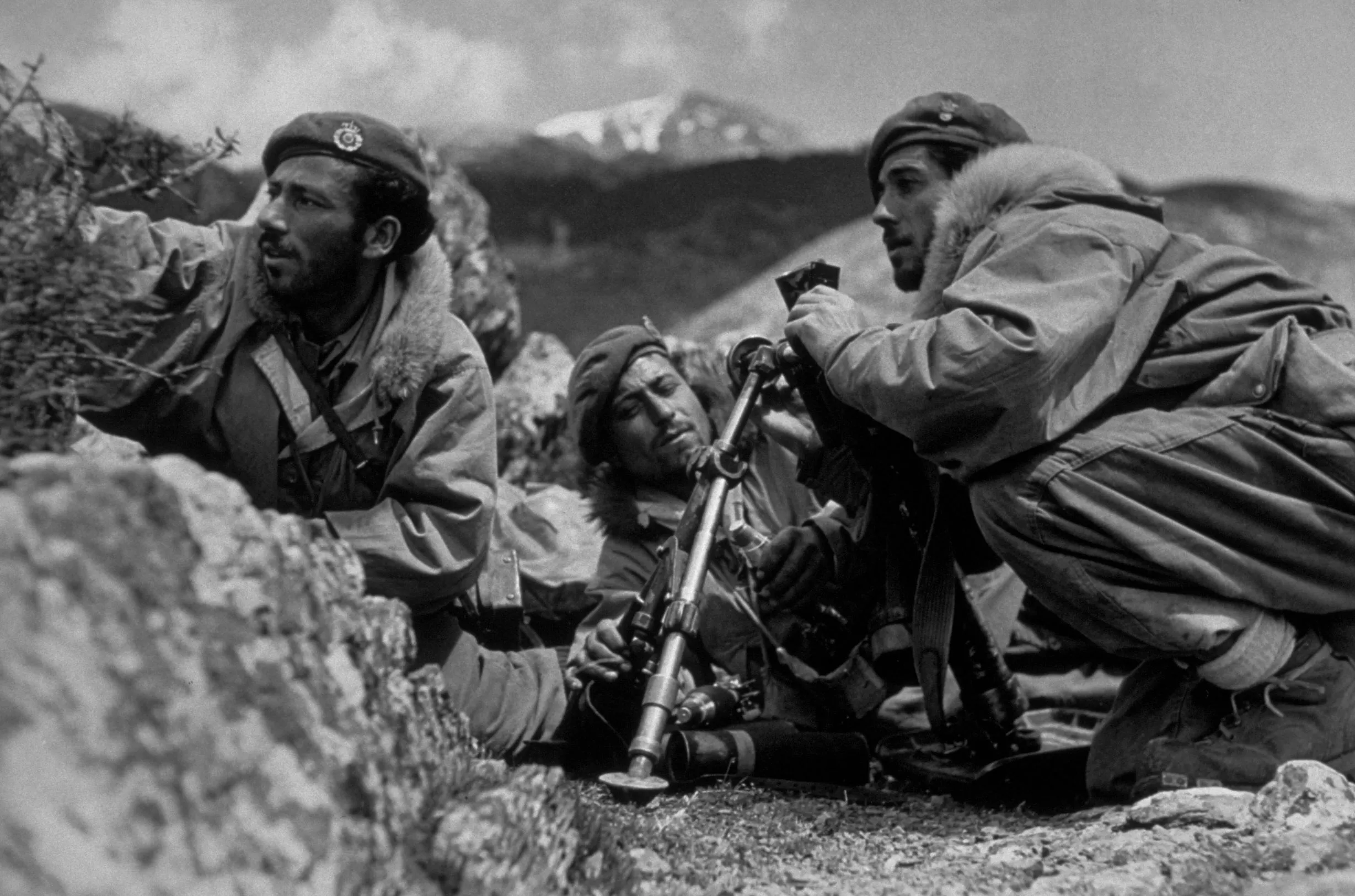 A black and white photograph of Greek soldiers laying on the ground ready for combat, holding weapons and looking in the distance.