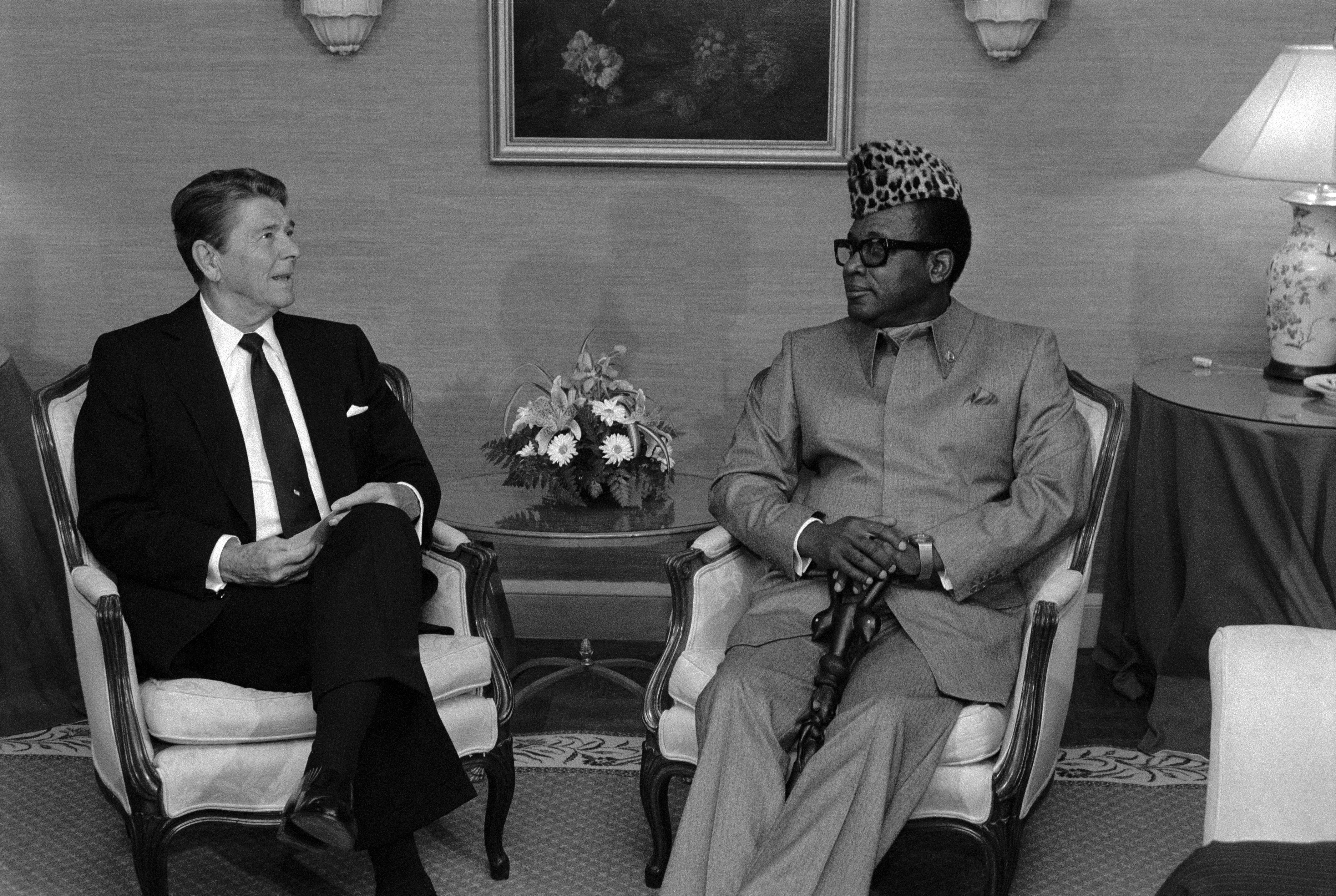 A black and white photograph of American President Ronald Reagan and President Mobuto Sese Seko of the Democratic Republic of the Congo seated in chairs. 