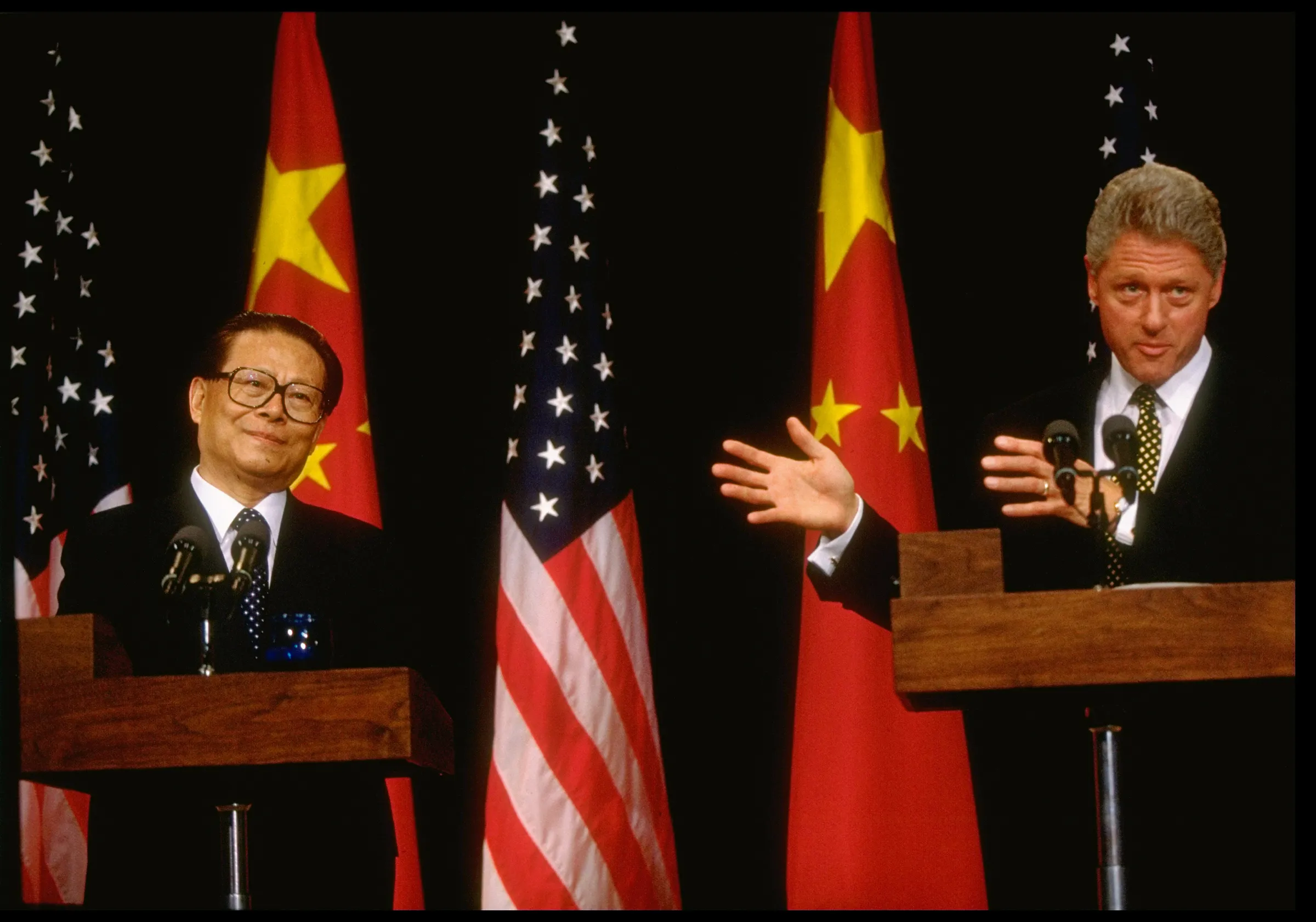 President Bill Clinton points to Chinese leader Jiang Zemin during joint press conference in front of U.S. and Chinese flags.